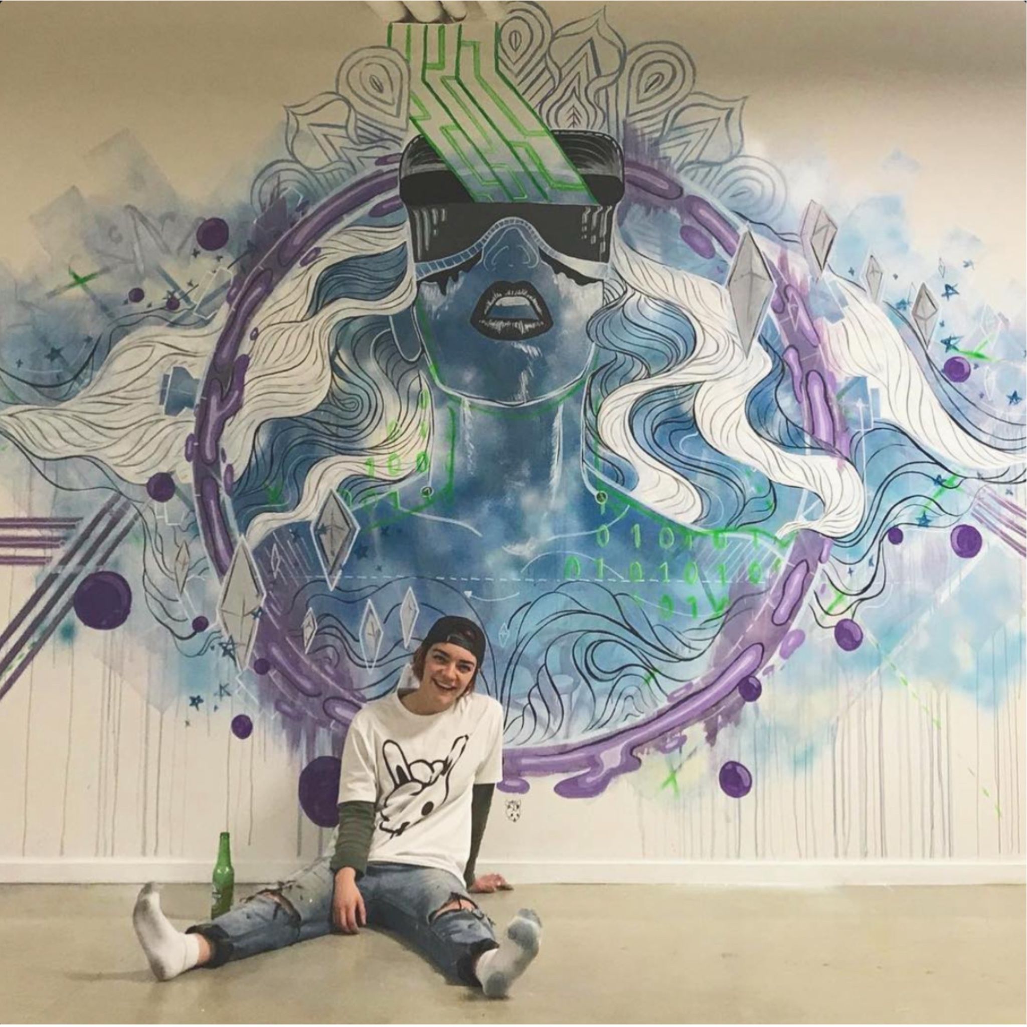 Bella sitting in front of a wall mural in swirling purples and blues of a woman, mouth open and hair blown back, in a VR set